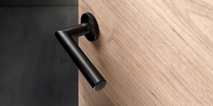 schwarzer Tuergriff in geradliniger Form an einer quergemaserten Holztuer